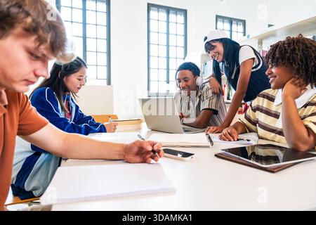 Multiethnic group of young students meeting at the library - diverse group of young students collaborating and studying with laptop and books around a Stock Photo