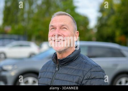 Portrait of a cheerful mature man in a dark jacket looking up with a joyful smile while standing outdoors on a cool day. Stock Photo