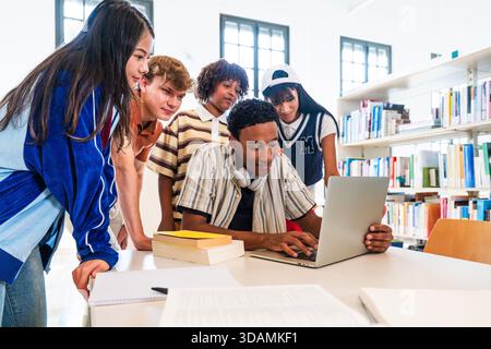 Multiethnic group of young students meeting at the library - young diverse students collaborating on project in a library, using laptop and textbooks Stock Photo