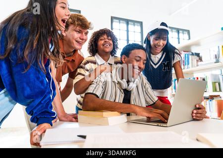 Multiethnic group of young students meeting at the library - diverse group of happy young students collaborating with laptop in a modern library. Shar Stock Photo