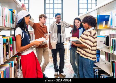 Multiethnic group of young students meeting at the library - multiethnic young students collaborating, learning, and reading books together in a moder Stock Photo