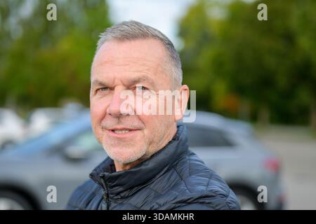 Portrait of a mature man wearing a black jacket, smiling confidently while standing outside on a cool autumn day. Stock Photo