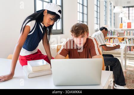 Multiethnic group of young students meeting at the library - young diverse students collaborating on project in university library, using laptop and b Stock Photo