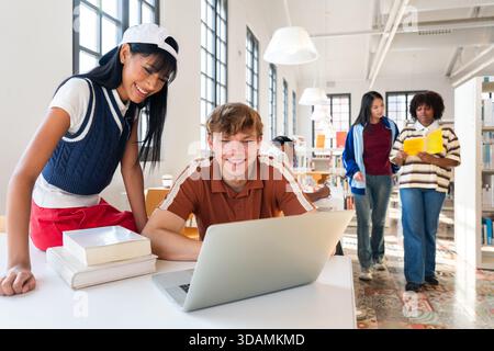 Multiethnic group of young students meeting at the library - young students smiling and collaborating in a university library, using a laptop for lear Stock Photo