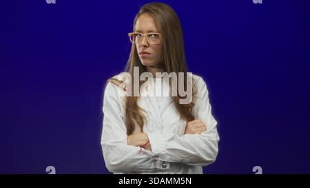 Woman scientist wearing lab coat and glasses with arms crossed in purple studio; frustration determination resilience. Stock Photo