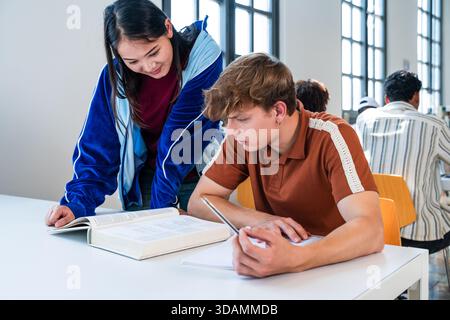 Multiethnic group of young students meeting at the library - young multiethnic students collaborating on an assignment, reading book and writing notes Stock Photo