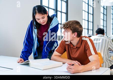 Multiethnic group of young students meeting at the library - young multiethnic students collaborating on a research project, reading a book and taking Stock Photo