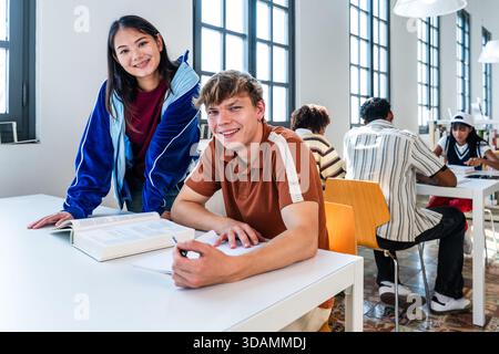 Multiethnic group of young students meeting at the library - young multiethnic students collaborating on a project and smiling at the camera, learning Stock Photo