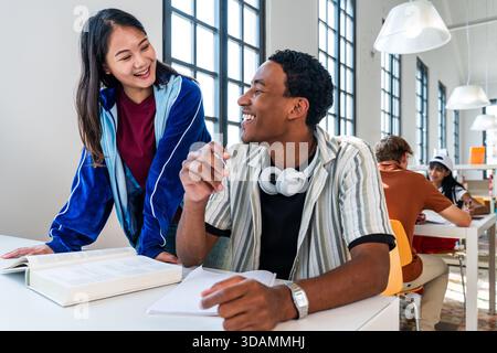 Multiethnic group of young students meeting at the library - diverse young adult students learning and interacting happily in a bright university libr Stock Photo