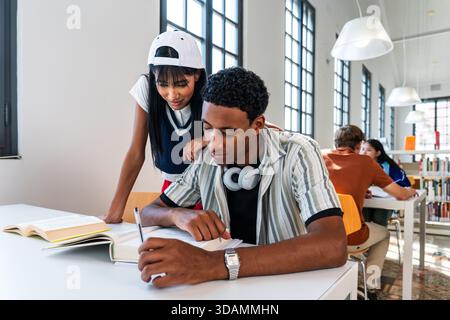 Multiethnic group of young students meeting at the library - young diverse students collaborating on a project, writing notes and reading books at a m Stock Photo