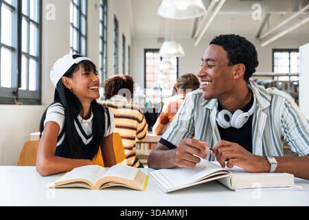 Multiethnic group of young students meeting at the library - young diverse students discussing and laughing while reading books in a university librar Stock Photo