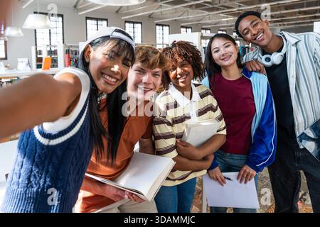 Multiethnic group of young students meeting at the library - diverse young students smiling for a selfie together inside a modern university library, Stock Photo