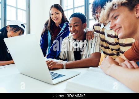 Multiethnic group of young students meeting at the library - group of diverse young students collaborating on laptop, smiling and studying together in Stock Photo