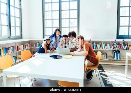 Multiethnic group of young students meeting at the library - young diverse students collaborating on a laptop and tablet, learning together in a brigh Stock Photo