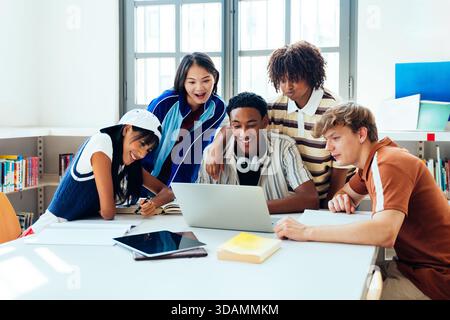 Multiethnic group of young students meeting at the library - multiethnic group of young classmates collaborating on school project using a laptop and Stock Photo