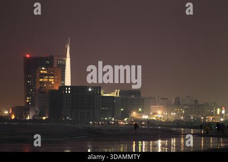 View of illuminated buildings reflecting on the water's edge under a dim sky, creating a captivating contrast of light and shadow, Karachi, Sindh, Pak Stock Photo