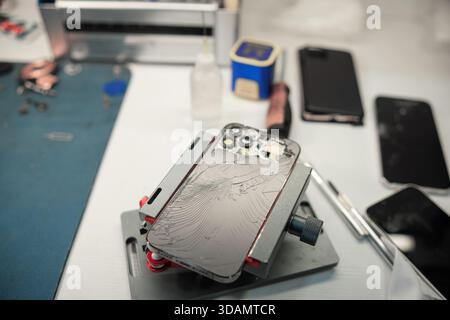 Tech Repair Process Occurs at a Workstation With a Broken Phone Being Fixed During the Day in a Busy Repair Shop Stock Photo