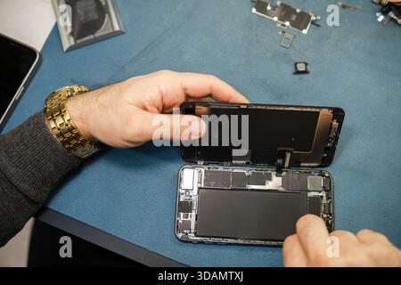 Technician Repairs Smartphone on Blue Work Surface With Tools and Parts Scattered Around During Daytime Work Hours Stock Photo