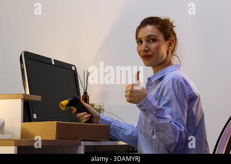 Staff in logistics point thumbs up while directing scanner toward box on work surface. Stock Photo