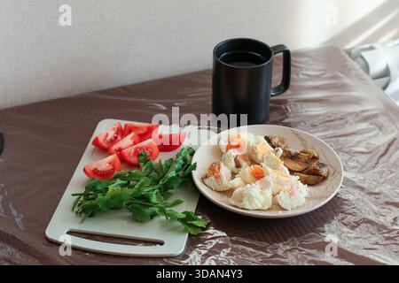 Everyday meal setup including boiled ingredients salad, herbs, tomatoes, and black mug in home setting Stock Photo