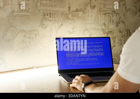 Close-up of fingers typing on keyboard while screen shows critical system error in blue Stock Photo