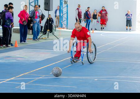 Male athlete with disability in a racing wheelchair in action, chasing the ball near the floor during a game on an indoor court. Stock Photo