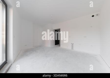 Interior of a newly built apartment without furniture. Empty room with white walls, grey concrete floor, plumbing pipes and electrical sockets. Space Stock Photo