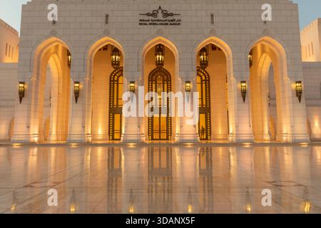 A twilight view of the Royal Opera House Muscat, showcasing its elegant architecture and glowing lights reflected on the polished courtyard. Stock Photo