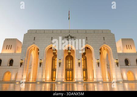 A twilight view of the Royal Opera House Muscat, showcasing its elegant architecture and glowing lights reflected on the polished courtyard. Stock Photo