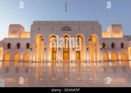 A twilight view of the Royal Opera House Muscat, showcasing its elegant architecture and glowing lights reflected on the polished courtyard. Stock Photo