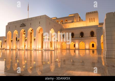A twilight view of the Royal Opera House Muscat, showcasing its elegant architecture and glowing lights reflected on the polished courtyard. Stock Photo