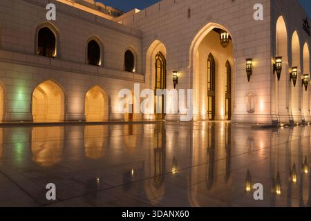 A twilight view of the Royal Opera House Muscat, showcasing its elegant architecture and glowing lights reflected on the polished courtyard. Stock Photo