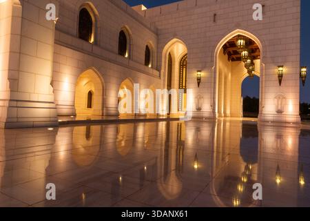 A twilight view of the Royal Opera House Muscat, showcasing its elegant architecture and glowing lights reflected on the polished courtyard. Stock Photo