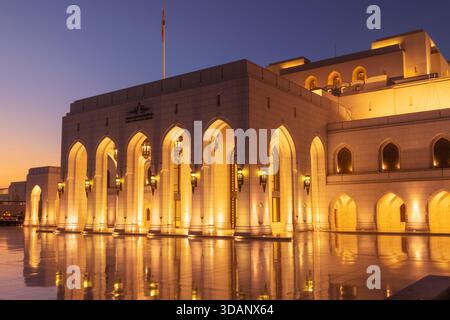 A twilight view of the Royal Opera House Muscat, showcasing its elegant architecture and glowing lights reflected on the polished courtyard. Stock Photo