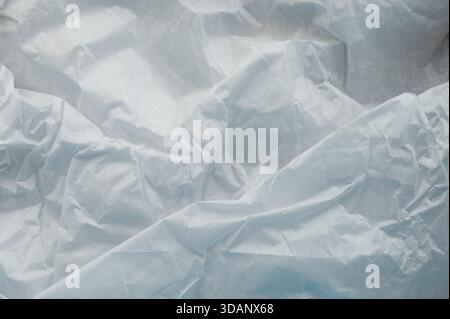 Crumpled white paper lies on a surface under bright light during the day, showing irregular folds and textures. Stock Photo