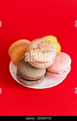 5 pastel-colored macaroons stacked on a white plate on a bright red background Stock Photo