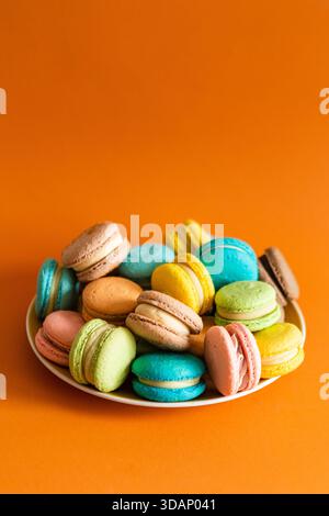 Large round plate full of colorful macaroons on an orange solid background Stock Photo