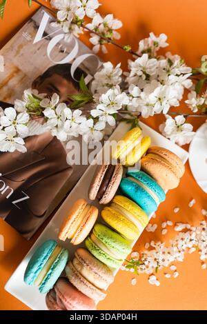 Many classic macaroons on white dishes, on an orange background in natural light Stock Photo