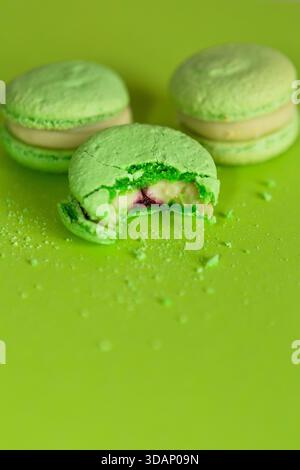 several green macaroons on a green background, one of them is bitten and crumbs are scattered around Stock Photo