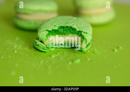 several green macaroons on a green background, one of them is bitten and crumbs are scattered around Stock Photo