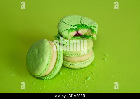 several green macaroons on a green background, one of them is bitten and crumbs are scattered around Stock Photo