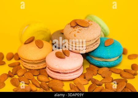 a bunch of macaroons of different colors on a yellow background, with scattered almonds all around Stock Photo