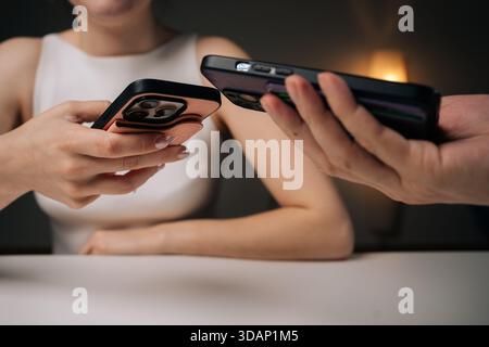 Two people exchanging data using mobile phones sitting at white table at home. Man and woman comparing smartphone data, sharing digital information Stock Photo