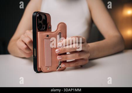 Woman holding sleek smartphone, featuring trendy protective case with hand strap, providing secure hold and contemporary style sitting at white table Stock Photo