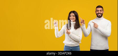 Two People Smiling and Pointing at Something on a Bright Yellow Background Stock Photo