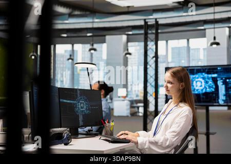 Smiling junior IT specialist writing code, developing machine learning APIs. Upbeat young female technician working in office, troubleshooting software errors using artificial intelligence tech Stock Photo
