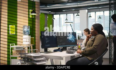 Jolly female programmer at office desk pleased after developing application using machine learning automation. Joyous employee satisfied after debugging applications using neural networks, camera A Stock Photo