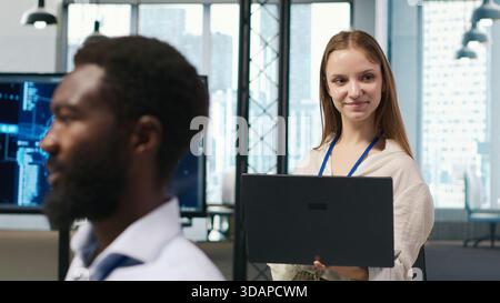 Portrait of young smiling female programmer in office automating repetitive tasks using AI scripts. Cheerful junior developer using artificial intelligence to speed up feature implementation, camera A Stock Photo