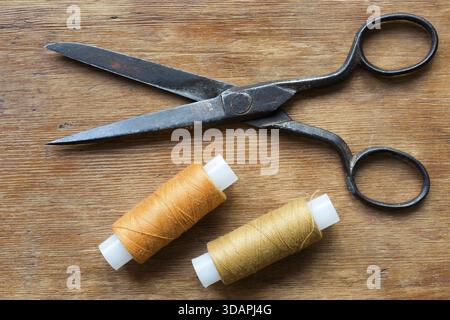 Vintage scissors on the red wooden background with two spools of threads Stock Photo