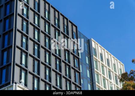 The exterior of a contemporary high-rise building with a grid of windows on contrasting dark and white panels under a clear blue sky. Stock Photo